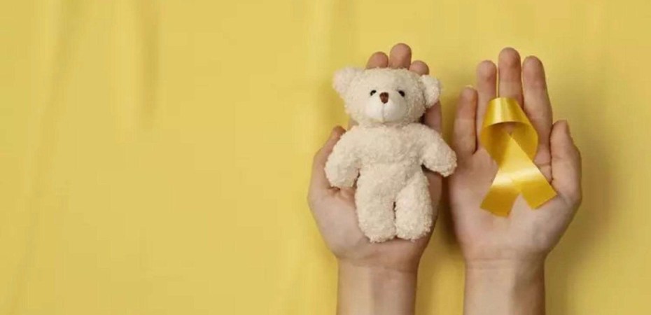 Fundo amarelo, um ursinho e o laço, símbolos da campanha de conscientização para a prevenção do câncer infantil